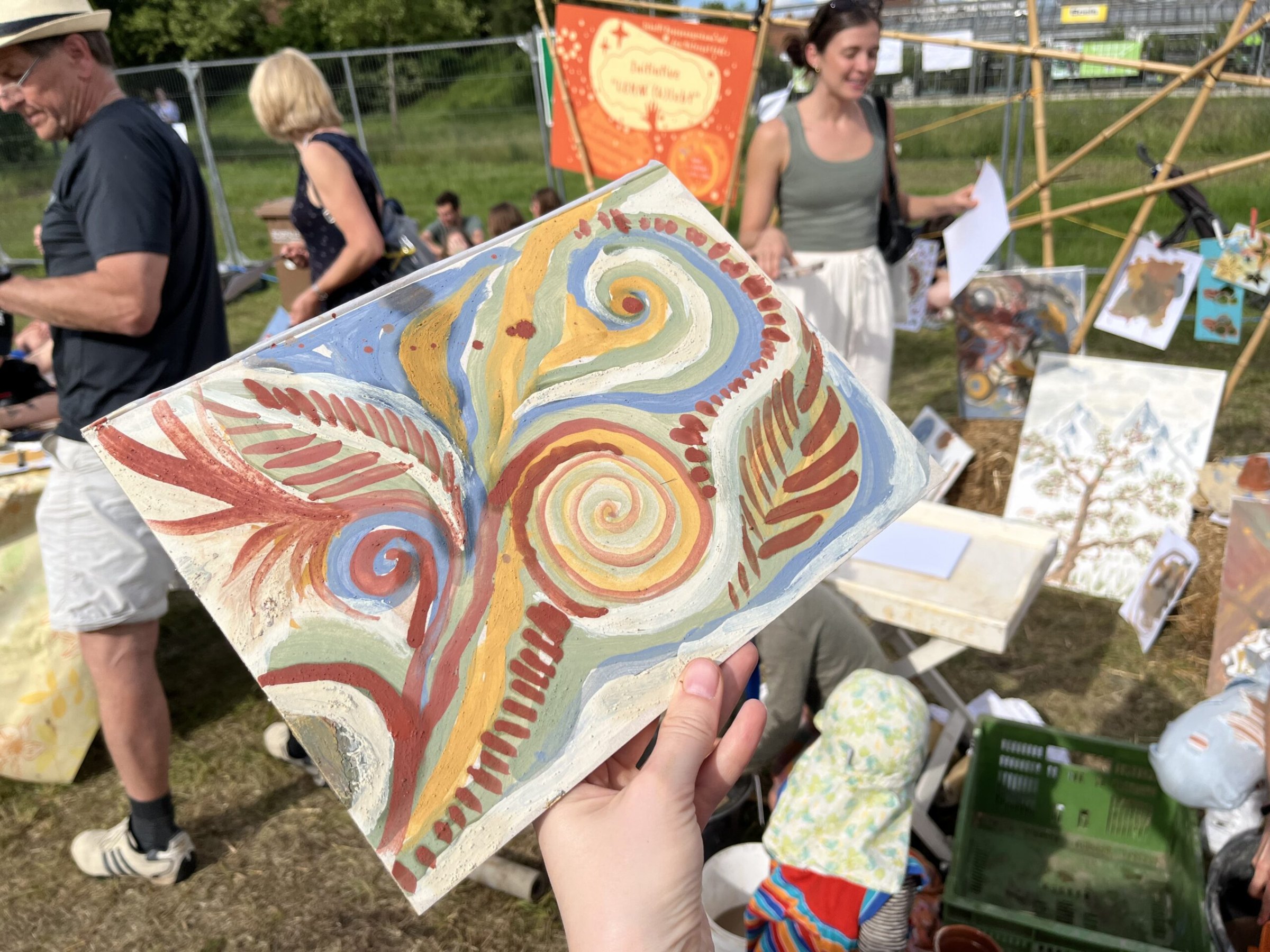 Ein Bild mit weichen Spiralen in zarten Erdtönen wird bei einem Fest in die Höhe gehalten