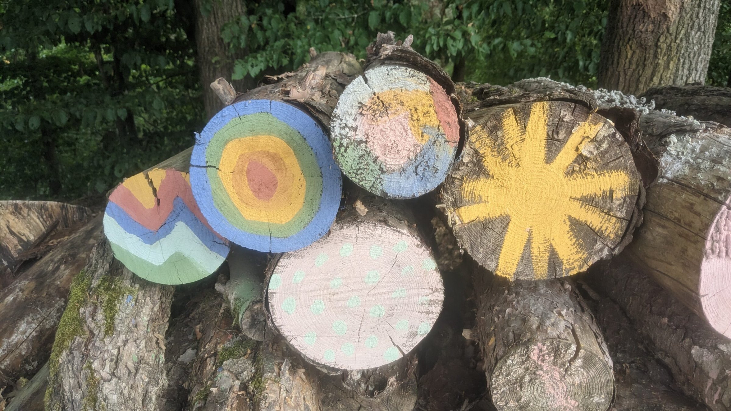 Baumstammscheiben mit bunten Kreide-Mustern aus Lehm: Ringe, Wellen und eine Sonne