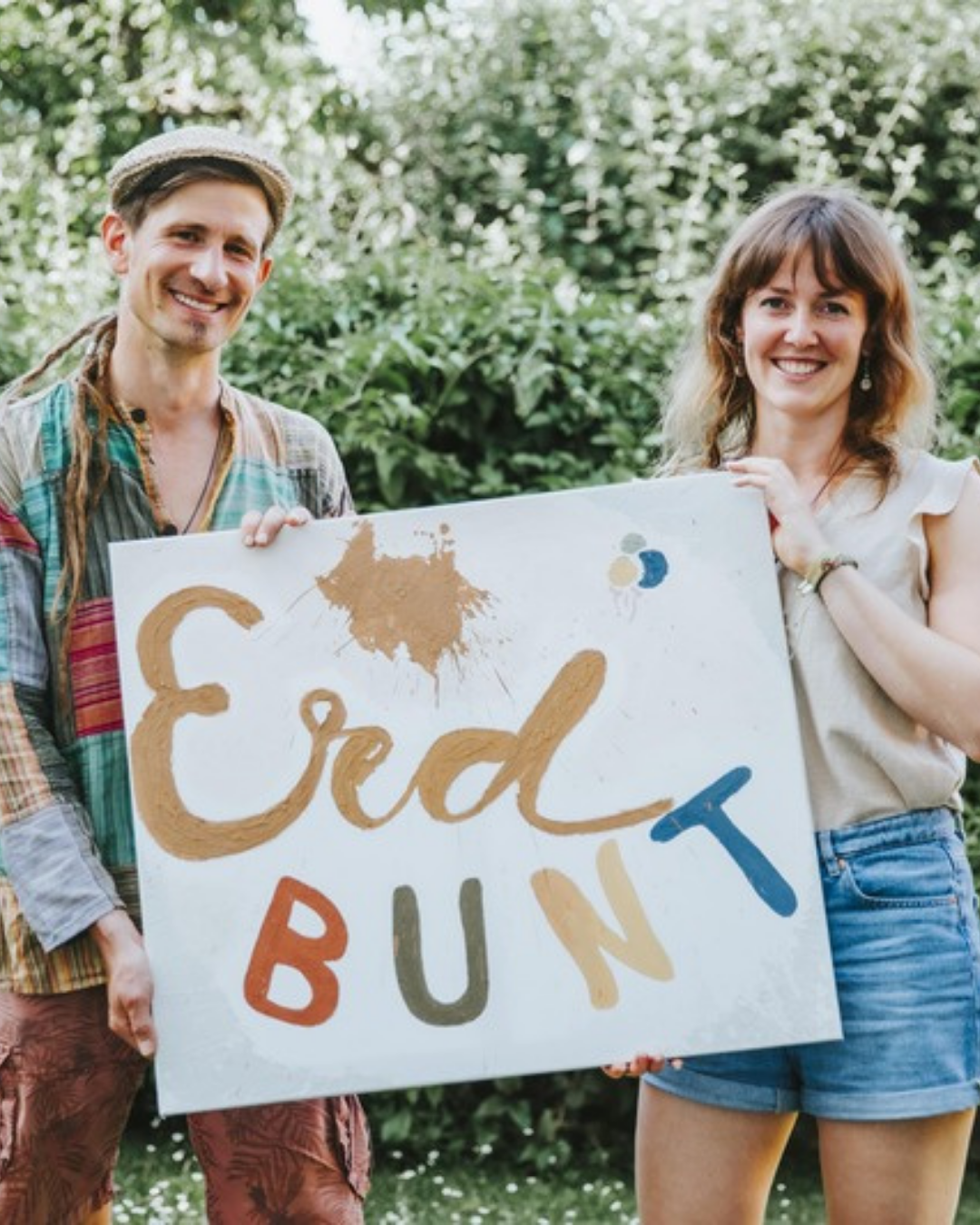 Anna und Harald halten lachend eine Leinwand mit dem handgemalten ErdBUNT-Schriftzug