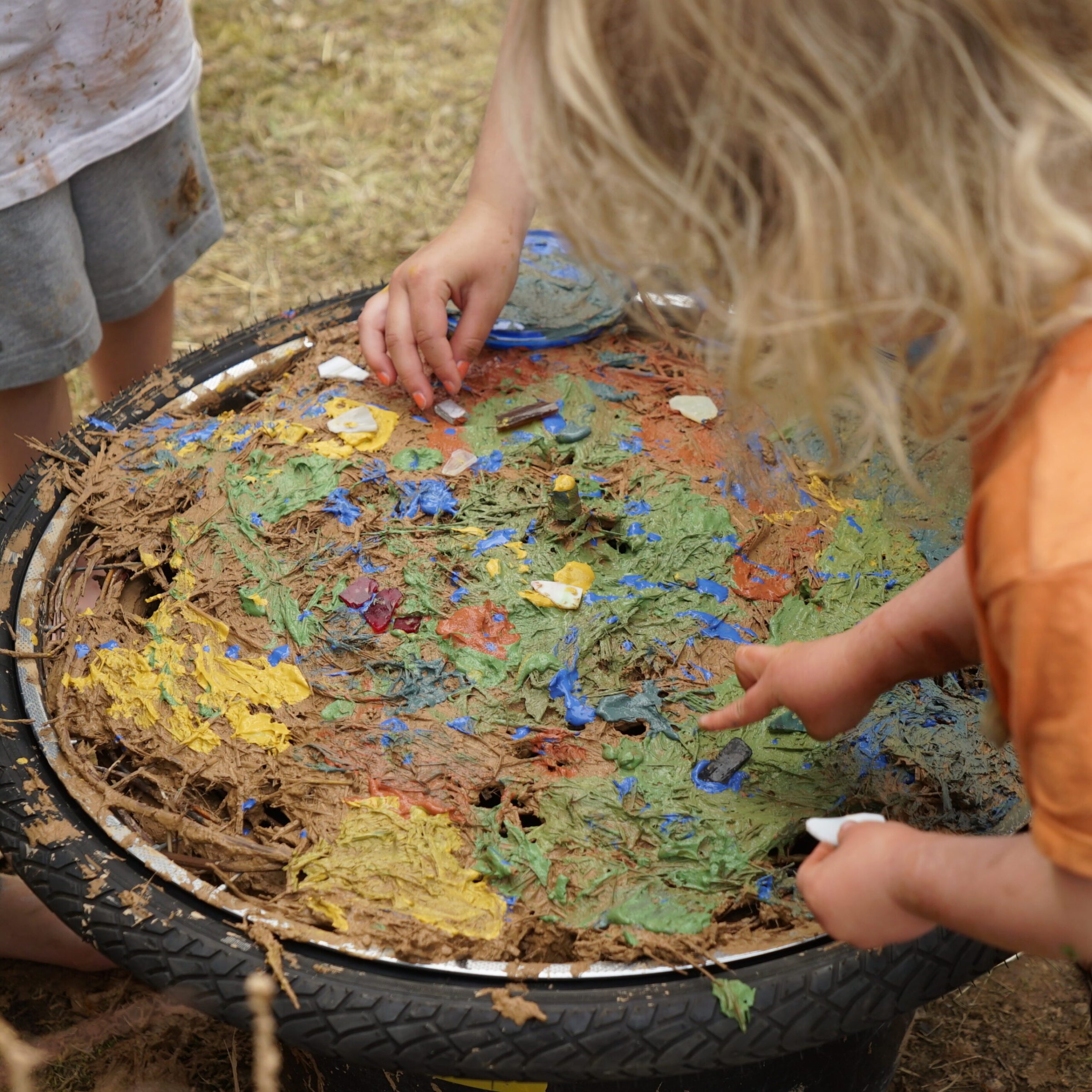 Kinderhände gestalten eine bunte Fläche aus Lehm und Farbe in einem alten Reifen