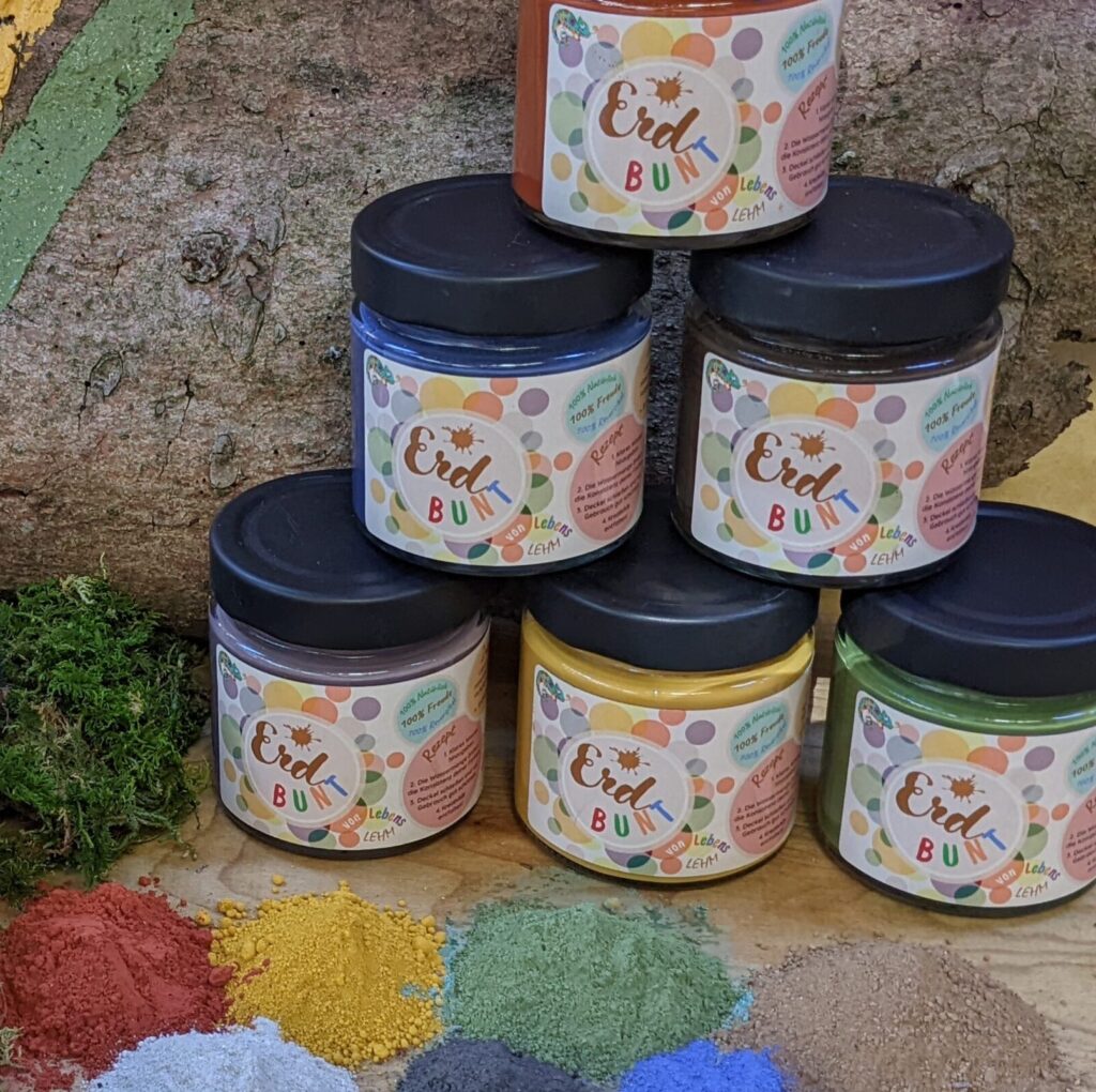 Häufchen aus rotem, gelbem, grünem und blauem Farbpulver vor ErdBUNT-Gläsern