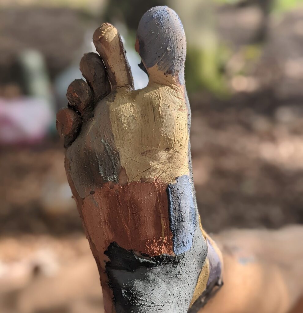 Ein Fuß, bunt bemalt mit Lehmfarbe in Gelb, Rot, Blau und Schwarz