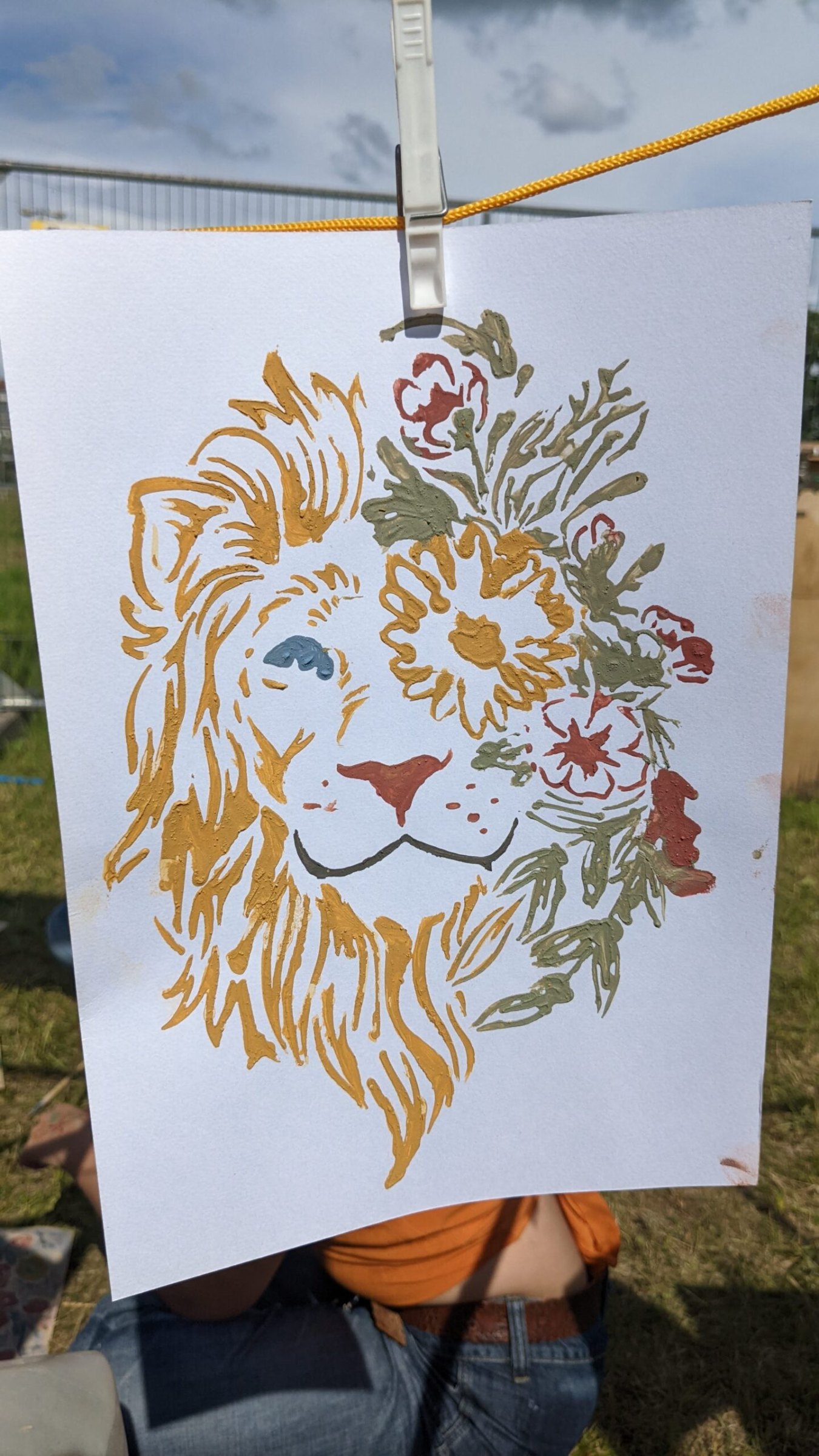 Ein mit Lehmfarben gemalter Löwenkopf mit Blumen hängt an einer Leine